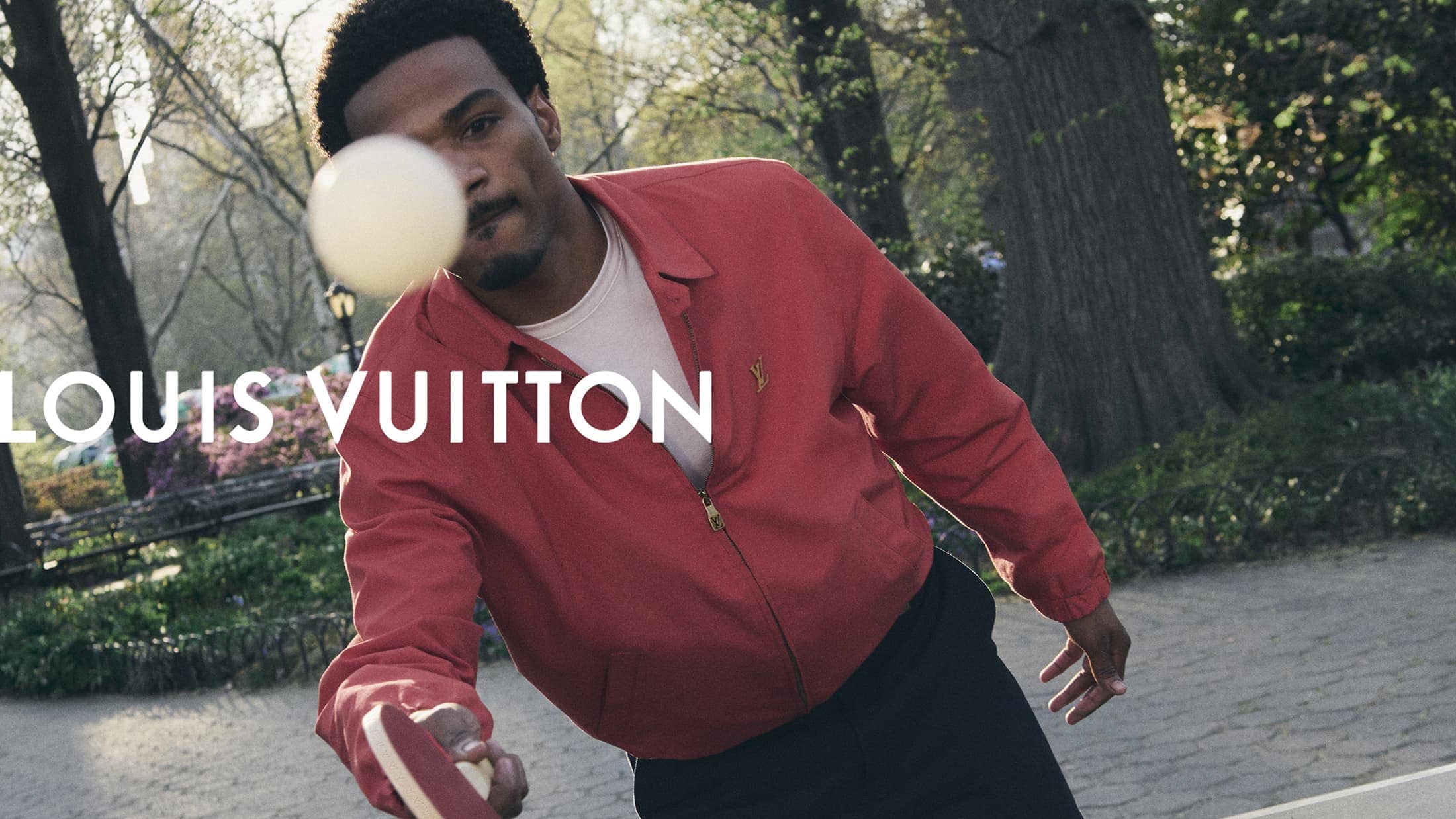 Young man in Louis Vuitton jacket playing with a ball outdoors.