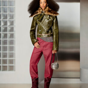Elegant woman wearing a green leather jacket with fur collar, red trousers, and boots, holding a sma.
