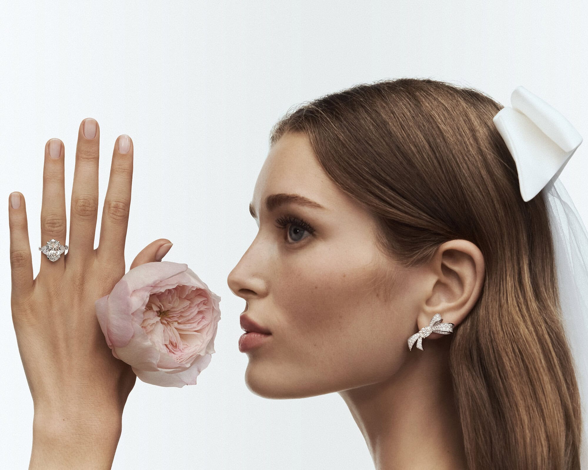 Woman with diamond ring, earrings, and a pink flower close-up.